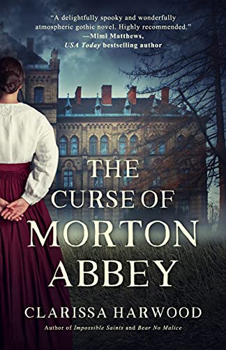 The Curse of Morton Abbey's Bookcover. Woman standing with her hands behind her back looking at a Victorian Gothic Manor House in early dusk.